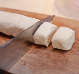 Скатайте тесто в «колбаску» (толщиной около 4 см). Разрежьте ножом примерно на 7 частей.
Обваляйте сырники в муке.