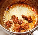 В небольшую кастрюльку насыпьте сахар, добавьте 2 ст.л. воды и доведите до кипения. Затем добавьте оставшиеся орехи и готовьте еще примерно 2-3 минуты. Сахар начнет карамелизироваться, и орехи будет покрываться карамелью. Уберите орехи с кастрюли и выложите пока на тарелку отдельно друг от друга (чтобы не слиплись).	