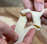 Один конец теста проденьте внутрь (как на картинке). Должно получиться подобие бантика. Проделайте тоже самое с остальными полосками.	