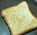 Обжарьте на сковороде на сливочном масле хлеб с двух сторон до легкой корочки. Намажьте хлеб сливочным сыром с одной стороны и нарежьте хлеб на квадратики (примерно 2 на 2 см).	