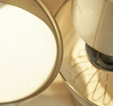 Затем добавьте горячее молоко и опять взбейте.  
Полученную массу перелейте в кастрюлю с толстым дном и готовьте на слабом огне, постоянно взбивая, до загустения массы. Должен получиться густой крем. Уберите с огня.	