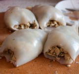 Разогрейте духовку до 200 градусов. Тщательно вымойте тушки кальмаров и начините их грибным фаршем. 
Смажьте кальмаров маслом и выложите их в форму для выпечки. Поставьте форму в духовку на 20 минут.	