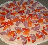 Порежьте оливки, перец, помидоры и колбасу, натрите на крупную терку сыр, мелко порубите зелень. Послойно выложите начинку на пиццу.