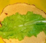 Приготовим соус, для этого смешаем сметану и красный молотый перец до однородного цвета. Тортилью подогреем на сковородке с двух сторон. На тарелку выкладываем тортилью, сверху укладываем лист салата.