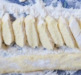 Добавляем к массе 150 грамм муки, вымешиваем тесто. На разделочную лоску высыпаем остатки муки, порциями выкладываем тесто и формируем продолговатую колбаску, не сильно обваливая ее в муке. Нарезаем творожистую колбаску поперек небольшими ломтиками в пол сантиметра.