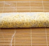 Приподнимаем край макису, придерживая пальцами начинку, начинаем скатывать ролл. Формируем ролл, усиливая нажим на циновку, движением рук от центра к краям макису.