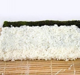 Смачиваем руки в рисовый уксус, берем готовый рис и распределяем по листу нори плотным ровным слоем, оставляя дальний от вас край на 1 см без риса.