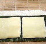 Переворачиваем лист нории таким образом, чтобы рис оказался внизу. Берем квадратные сырные кусочки и укладываем по поверхности заготовки.