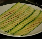 В небольшую пиалу выдавливаем 2-3 зубчика чеснока и заливаем 2 столовыми ложками растительного масла. Даем немного настояться. На огонь ставим сковороду гриль, когда она хорошо разогревается, тонким слоем смазываем ее чесночным маслом и выкладываем полоски цукини. Кабачок так же смазываем поверху тем же маслом и немного солим. Когда коричневые полоски от гриля начали проявляться сверху, снимаем цукини со сковороды (со второй стороны не жарим).