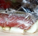 Наутро в рукав укладываем порезанный на крупные куски лук, целые зубчики чеснока, сверху выкладываем мясо, пару горошин душистого перца и лавровый лист.