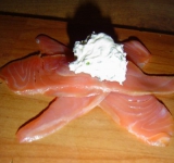 Нарезаем рыбу тонкими пластинами и выкладываем друг на друга три пластинки. В центр чайной ложкой помещаем творожный сыр с чесноком.