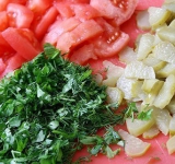 У помидоров удаляем кожицу и нарезаем их на дольки. Половину помидор добавляем к луку с морковью и продолжаем тушить овощи под крышкой еще 5 минут. Зелень измельчаем, огурцы нарезаем брусочками, если кожура толстая, а семечки большие, то огурцы стоит почистить, а семечки удалить.