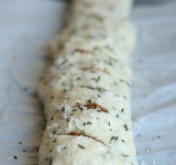 Заворачиваем узкие края теста и сворачиваем пласт в рулет, переносим его на противень. Делаем на рулете поперечные надрезы через 4-5 см. Смазываем поверхность рулета яйцом, посыпаем оставшимся сыром и мелко порубленной зеленью (орегано).