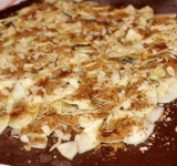 Пласт теста посыпаем бисквитной крошкой, отступив от края по паре сантиметров со всех сторон. Поверху выкладываем ломтики фруктов, посыпаем их сахаром, миндальными лепестками, корицей и изюмом.