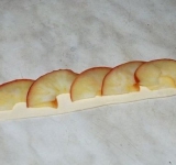 Тесто раскатываем до толщины в 1-2 мм, и нарезаем на полоски в ширину 3 см. На тесто внахлест выкладываем 5 яблочных лепестков, таким образом чтобы яблоки на 1/3 выходили закрай теста. Излишек теста по длине отрезаем, оставив запас по 1 см с каждой стороны.