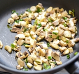 Нарезанный лук обжарьте на сливочном масле на сковороде в течении 1 минуты.  
В это время порежьте на кубики грибы и добавьте их к луку. Готовьте еще 2-3 минуты. Посолите и поперчите.	