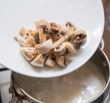 Грибы порежьте на кусочки и также добавьте в кастрюлю. Готовьте 2 минуту.