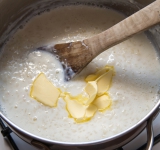 Добавьте оставшееся горячее молоко и сливочное масло. Перемешайте.  
Дальше есть несколько вариантов приготовления.  
а) накрыть крышкой и поставить в духовку (180 градусов) на 7 минут. 
б) готовить на пару также 7 минут 
в) завернуть в одеяло на 10 минут.  
Каша готова. Приятного аппетита!	