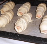 Выкладываем сосиски в тесте на противень, застланный бумагой для выпечки. Оставляем на 20 минут, чтобы тесто немного подошло.	