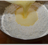 В мучной смеси в середине делаем лунку и выливаем туда взбитые яйца.