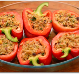 Помидоры обтираем бумажными полотенцами, сбрызгиваем оливковым маслом и выкладываем к перцам в форму для запекания. Ложкой наполняем овощи приготовленной начинкой и ставим в духовку на 20 минут.