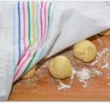 Получившееся тесто делим на 20 равных частей и скатываем их в шарики. Выкладываем шарики на просыпанную мукой рабочую поверхность, накрываем полотенцем и оставляем на 10 минут, для поднятия.