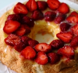 Нижний корж смазываем оставшейся частью лимонного курда и выкладываем пластинки клубники. Накрываем верхним коржом.