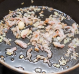 Нарежьте лук и бекон, чеснок очистите и порежьте пополам. Нагрейте сковороду с растительным маслом, положите туда лук, чеснок и бекон. Готовьте около 5 минут на слабом огне. Вытащите чеснок.	