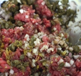 Перекладываем мясо в глубокую посуду, добавляем каперсы, измельченный лук и мелко порезанные анчоусы. Солим, перчим, приправляем уксусом и оливковым маслом. Все хорошо перемешиваем, накрываем пищевой пленкой и даем постоять в холодильнике 1 час.