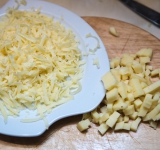 Половину сыра натрите на крупной терке, оставшуюся часть порежьте на средних размеров кубики.	
