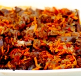 Для начала подготовим некоторые продукты: крупно нарежьте баранину, очистите и натрите морковку на крупной терке, крупно нарежьте лук и томаты. Разогрейте духовку. Поставьте на огонь глубокую сковородку и разогрейте на ней растительное масло. Добавьте лук и обжарьте до золотистого цвета. Затем добавьте морковку. Жарьте вместе минуты 2, а потом добавьте мясо, жарьте минуты 4-5, потом влейте вино, добавьте чеснок и помидоры. Хорошенько перемешайте продукты и тушите вместе до кипения. Снимите с огня. Переложите готовую начинку в форму, в которой будете запекать блюдо.