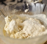 Для начала смешайте соду со сметаной. Растопите на огне масло и влейте его в сметану, тщательно перемешайте до однородности.
Теперь, продолжая перемешивать, постепенно всыпайте муку, небольшими порциями. Когда всыпете около 1.5 стакана муки, проверьте тесто руками. Если тесто будет липнуть к рукам, добавьте остальную муку. Если нет, то половину стакана можно оставить. Тщательно вымешайте тесто и разделите его на 2 равные части.