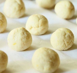 Для начала при помощи миксера хорошенько смешайте творог, желток и сахарную пудру. Растопите сливочное масло, слегка охладите его и влейте к творожной массе. Добавьте мед (если мед густой, то его тоже необходимо растопить на водяной бане). Хорошенько перемешайте все до однородной массы. Добавьте ванильную эссенцию. Ее можно заменить ванилином, но с ним осторожно, потому что он может горчить. Просейте муку, смешанную с разрыхлителем. Добавьте муку к творожной массе. Тщательно все перемешайте на низкой скорости.  
 
Выложите тесто на стол. Измельчите цедру лимона и добавьте ее к тесту, хорошенько обомните.  
Сделайте из теста длинную колбаску и разделите ее на 16 одинаковых частей.	