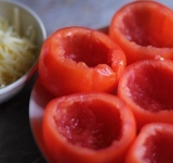 Разогрейте духовку. С помидор аккуратно срежьте верхушку при помощи острого ножа. Аккуратно выскребите мякоть при помощи чайной ложкой. Мякоть можете не выбрасывать, из нее можно приготовить отличный соус к пасте.	