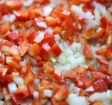 Лук и болгарский перец очистите и нарежьте на мелкие кусочки. Разогрейте сковородку с растительным маслом и обжарьте на ней лук и перец минут 10. Тем временем измельчите чеснок, добавьте его к перцу с луком и подержите на огне еще пару минут.  
 
Измельчите куриное филе и обжарьте его отдельно от овощей до полуготовности.	