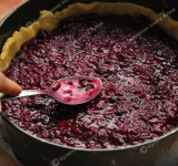 Разогрейте духовку. Форму для выпечки выстелите бумагой для запекания. Разделите тесто на 2 неравные части. Большую часть раскатайте скалкой (диаметр примерно 30 см) и выложите ее в форму, сформировав бортики.
Выложите сверху на основу начинку и аккуратно разровняйте ее.