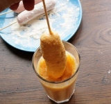 Для начала тщательно смешайте все сухие ингредиенты. Вбейте к сухой смеси яйцо, перемешайте, а затем, продолжая мешать, порциями введите молоко. В итоге должно получиться очень густое тесто. При необходимости добавьте немного муки или молока. Нанизайте сосиски на шпажки и обваляйте их в муке (чтобы тесто потом лучше держалось).
Перелейте тесто в широкий стакан. На разогретую сковородку налейте масло так, чтобы оно покрывало дно сковородки примерно на 2 см.