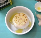 Для зачала подготовим чеснок. Острым ножом срежьте с головки чеснока верхушку, примерно 1 см. Переложите чеснок в маленькую мисочку и полейте оливковым маслом, а сверху накройте блюдцем. Разогрейте чеснок в микроволновке минуты две, пока он не размякнет. Тоже самое можно сделать и в духовке, но потребуется гораздо больше времени. Когда чеснок слегка остынет, выдавите и измельчите зубчики.