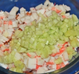 Измельчите чеснок, добавьте в салат. Огурец очистите от кожуры и мелко нарежьте, добавьте в миску.