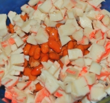 Для начала слейте всю жидкость с фасоли и выложите ее в миску. Крабовые палочки нарежьте на крупные кубички и добавьте к фасоли.