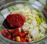 Мелко порубите петрушку. Помидор ошпарьте, очистите от шкурки и нарежьте на мелкие кубички. Перец (и сладкий, и горький) мелко нарезать. Измельчите лук. Мелко порубите чеснок. Все нарезанные ингредиенты добавьте к фаршу и добавьте туда же ложку соуса из сладкого перца (можно заменить томатной пастой. Добавьте специи и тщательно перемешайте до однородности. Если фарш будет очень плохо намазываться на лепешки, то можно будет добавить в него немножко воды.