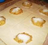 Тесто разморозим, немножко раскатаем и порежем на квадратики. Приготовим начинку: бананы натрем на крупной терке, разложим на тесто, а сверху на каждый кусочек теста насыплем по ложке сахара.